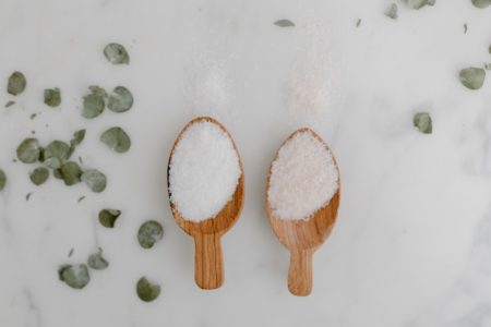 Deux grandes cuillères posées sur un fond blanc marbré : l'une contient du sel et l'autre du sucre. Une illustration des différents types de sel et de sucre